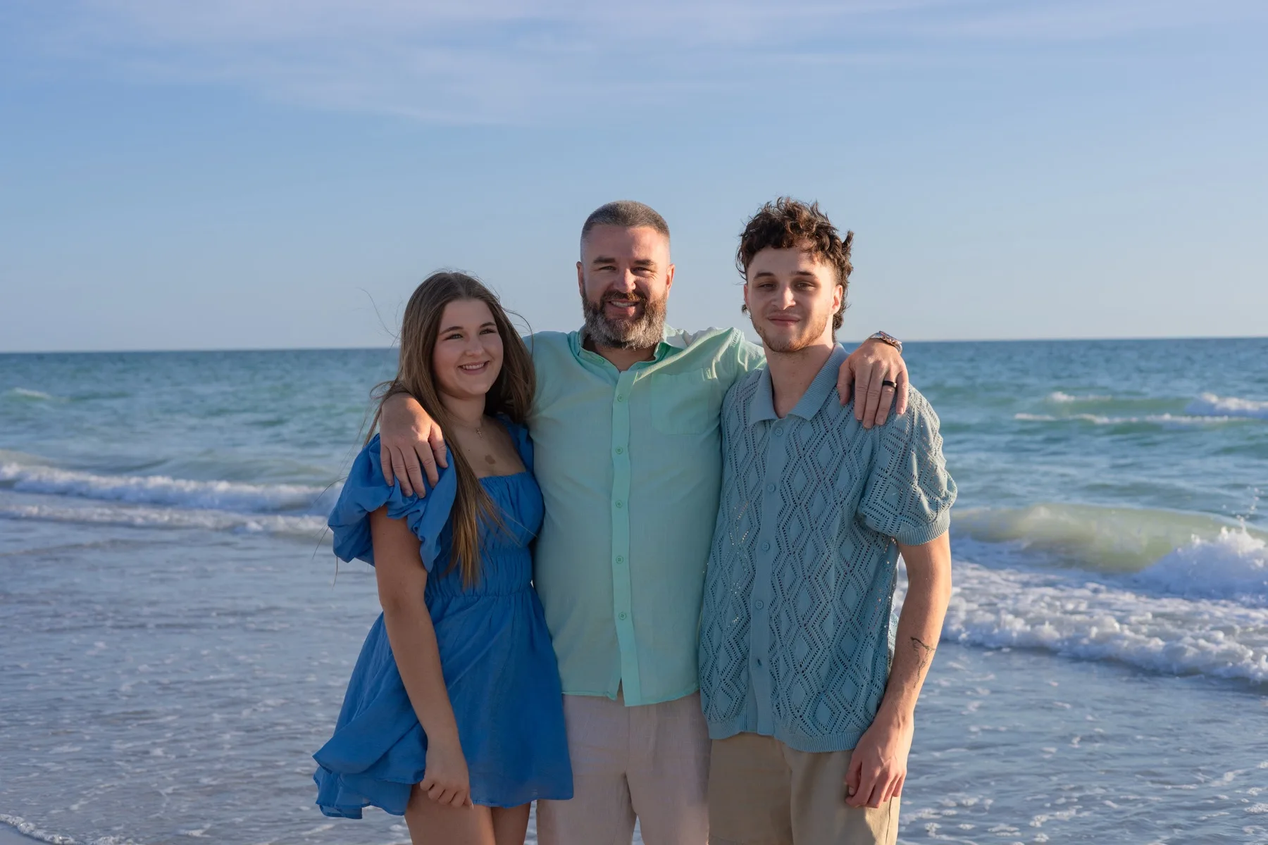 Father held by his two grown children at the shore.