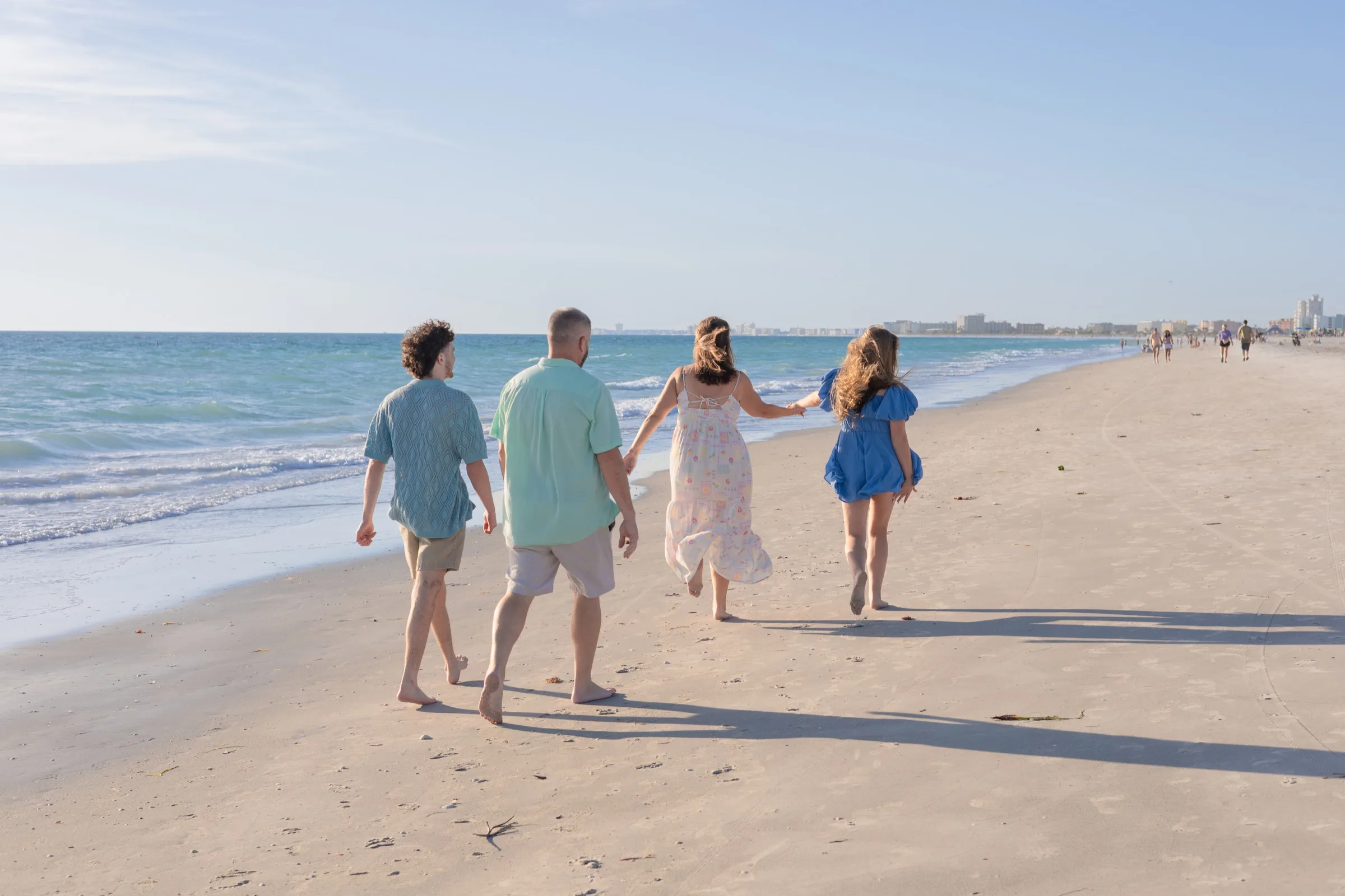 Family of four walking together along the soft sand of a Florida beach in late-afternoon light, holding hands.